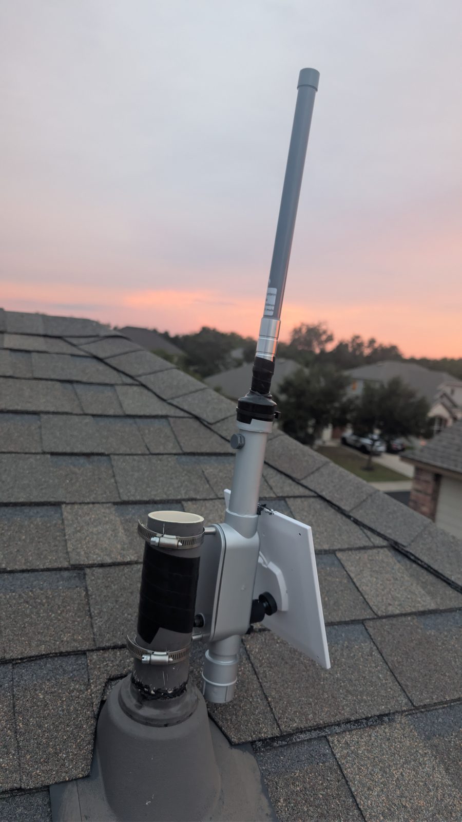 A finished conduit-body repeater on a roof at sunset, with a tall fiberglass antenna and a solar panel on the side.