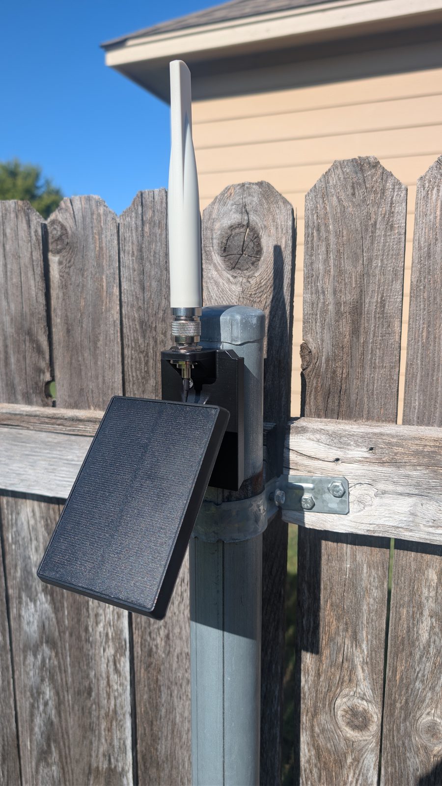 The finished repeater on a steel fence post, a white antenna on top and its solar panel angled out to the side.