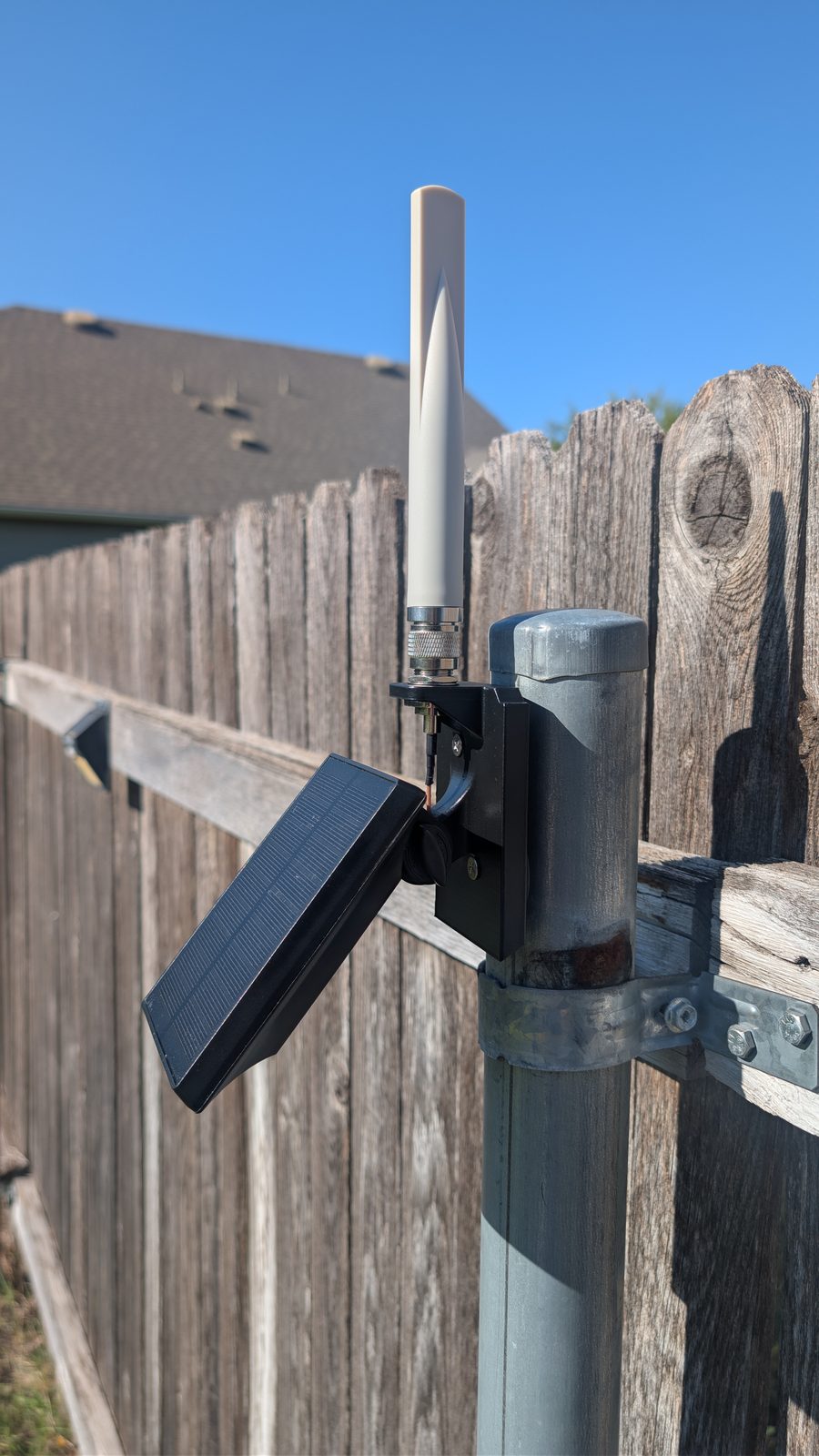 The repeater seen from the side on a steel fence post, its printed mount holding the housing and the solar panel on its arm.